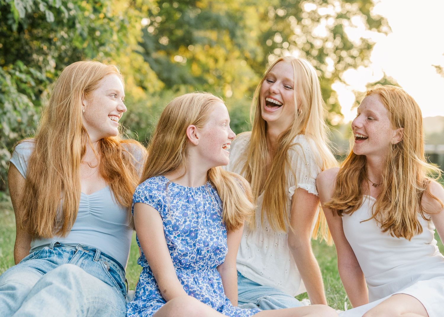Four siblings share a candid laughing moment together during an outdoor photo session.