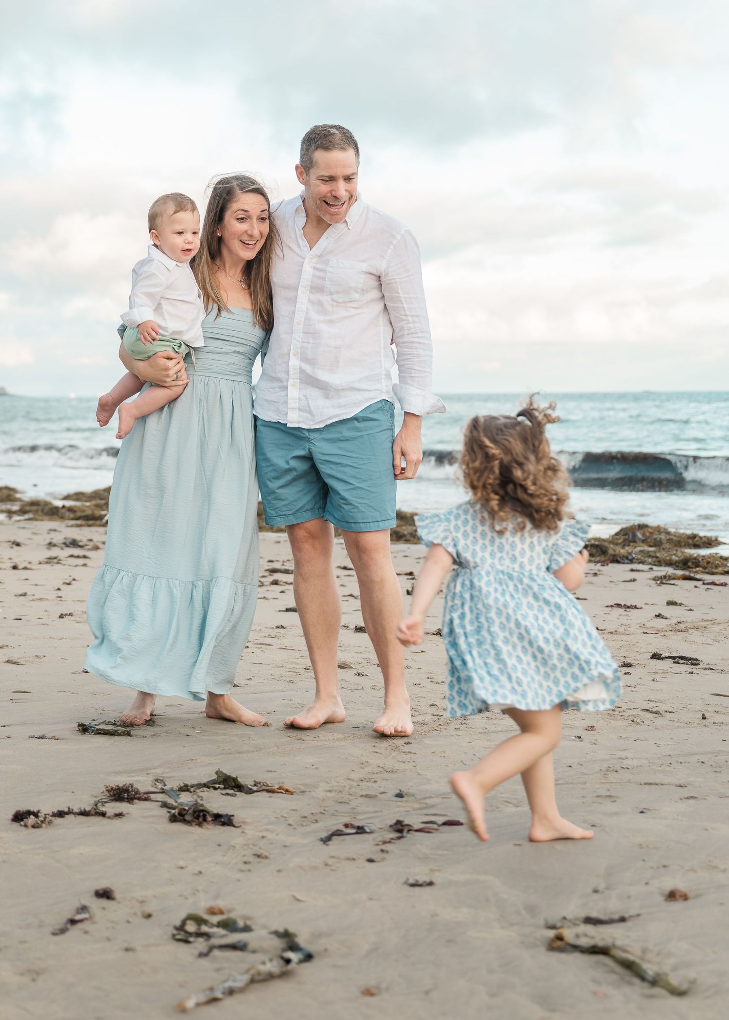 A family enjoys a carefree moment on a scenic beach as a carefree child dances by the ocean waves.