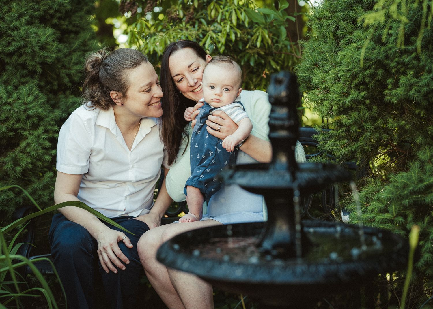 A family moment captured by a decorative garden fountain with lush greenery.