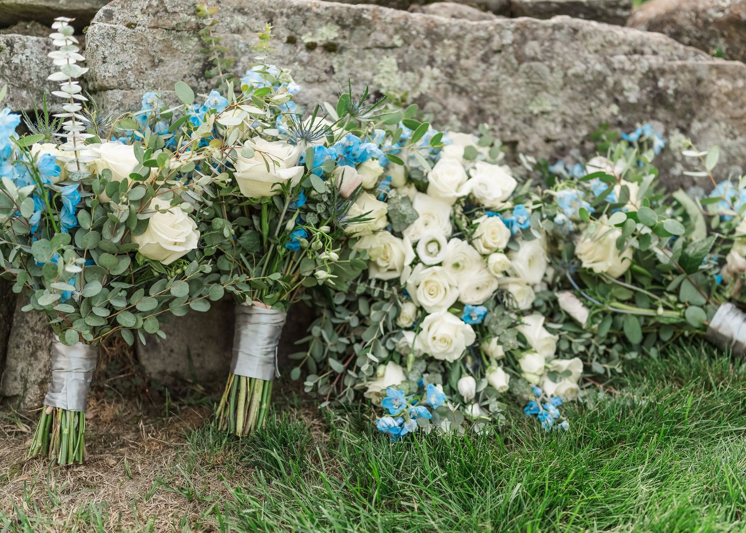 Beautiful white roses and turquoise floral arrangements line a rustic stone wall, creating an elegant outdoor display.