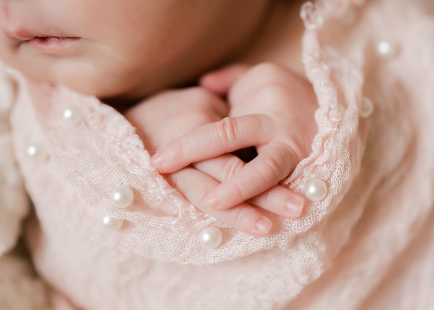 Close-up of tiny baby hand resting on delicate lace fabric.