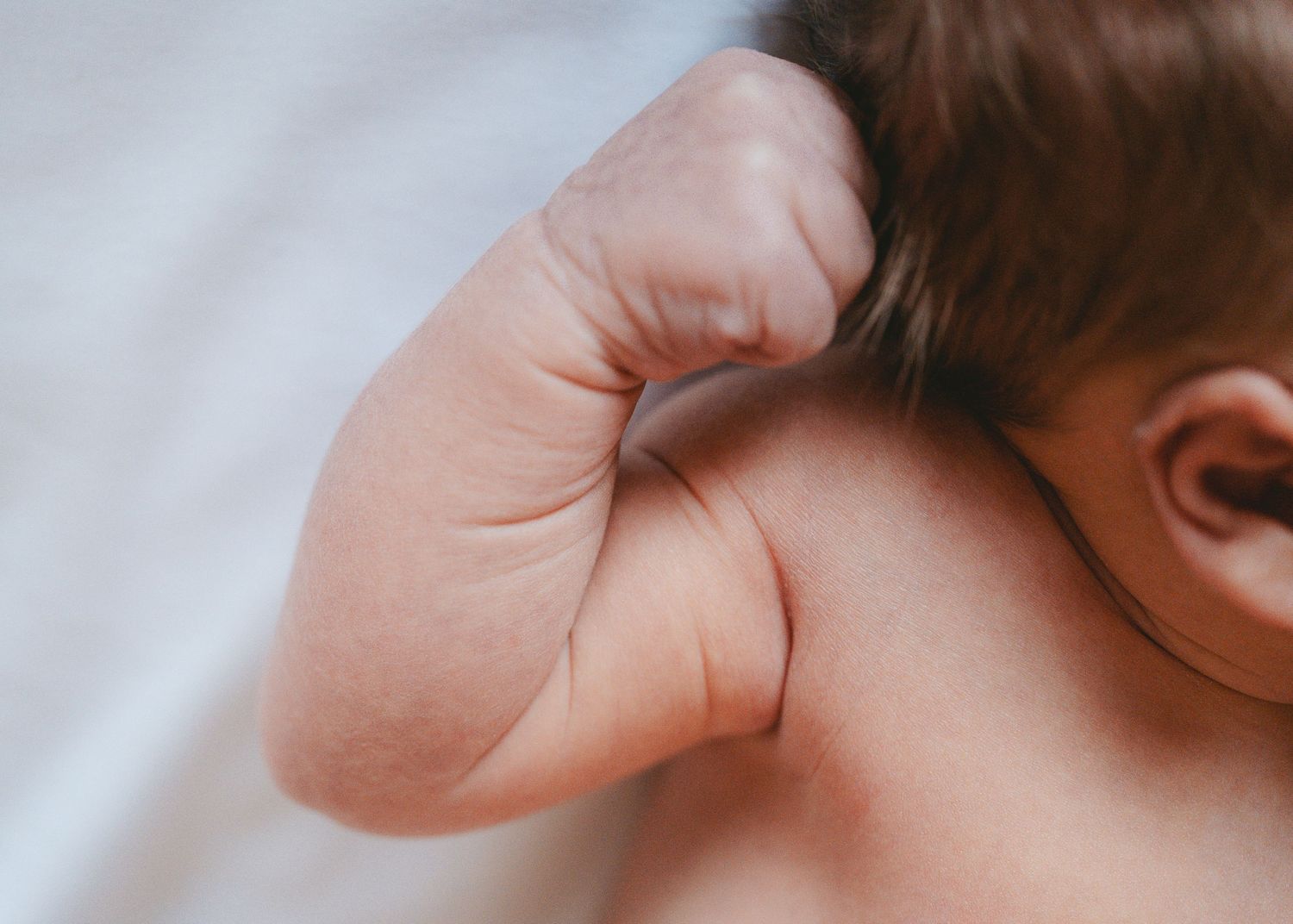 Close-up of baby's ear and hair against white fabric.
