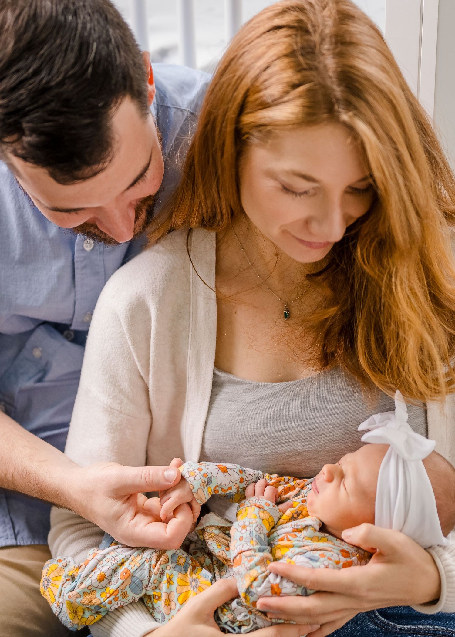 Parents bonding with newborn wearing floral outfit on couch.