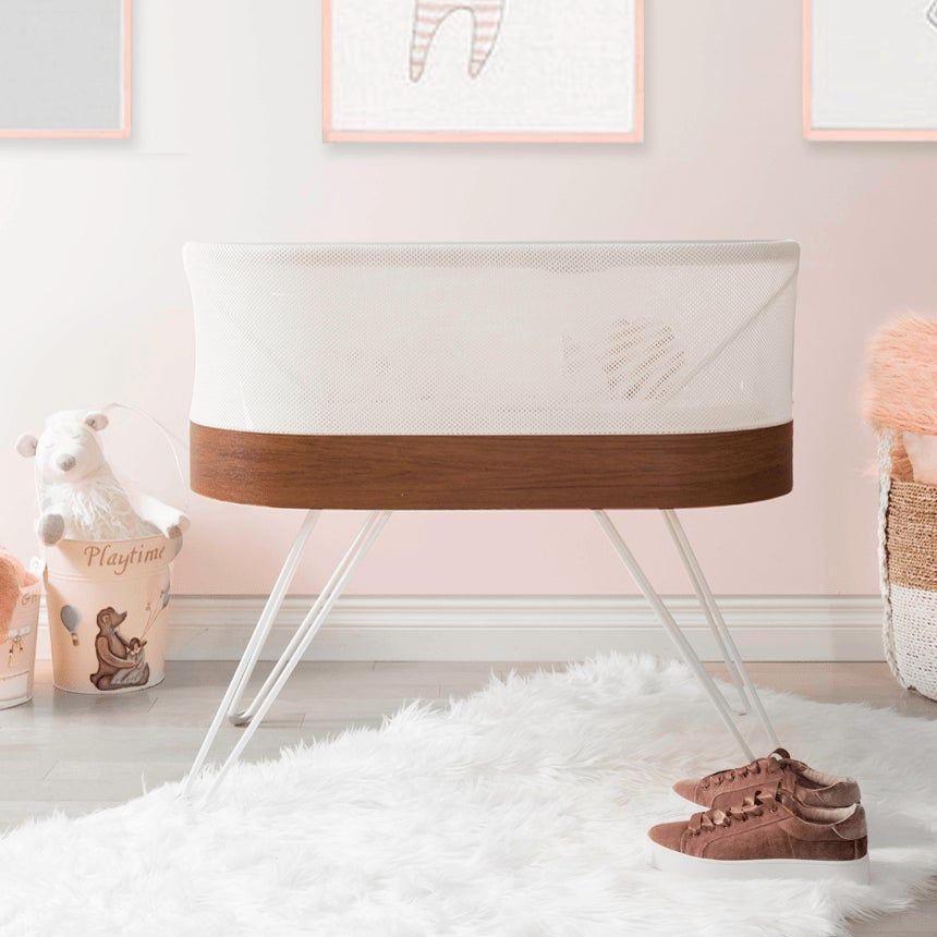 Modern white and wood baby bassinet with clear acrylic legs in a minimal nursery setting.