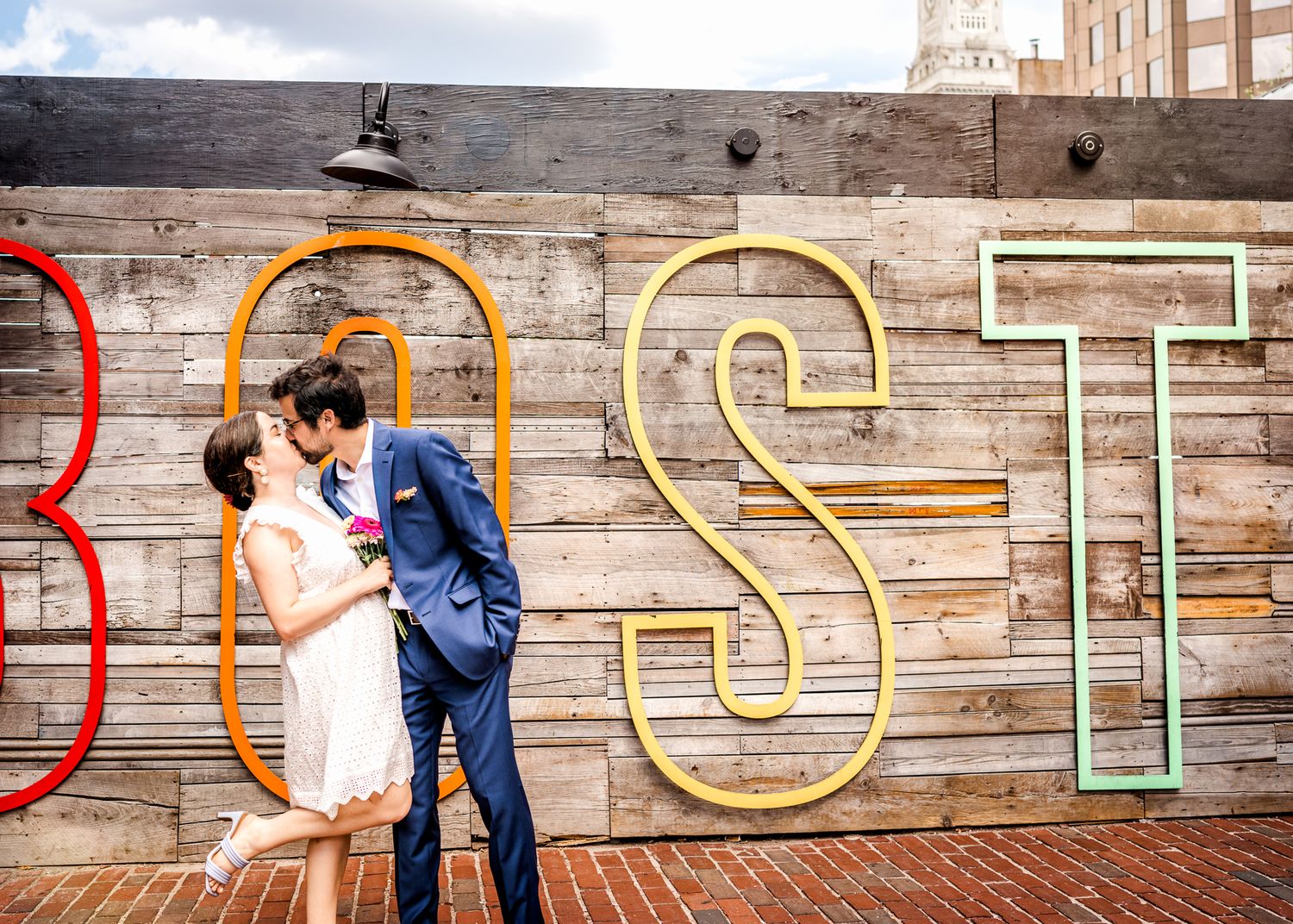 Romantic moment shared between couple in front of rustic Boston wall art.