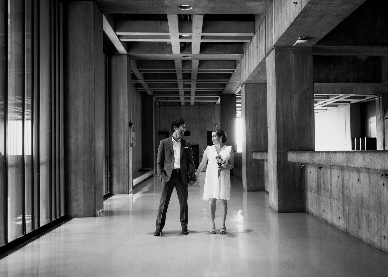 A couple walks together in a modern building hallway in black and white.
