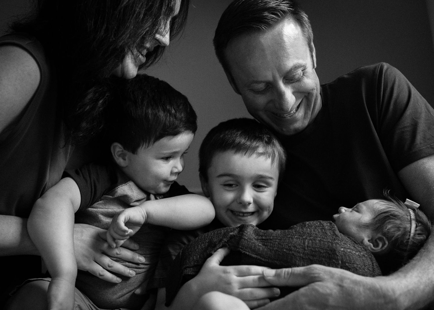 Black and white portrait of a family sharing an intimate moment together with a newborn baby.