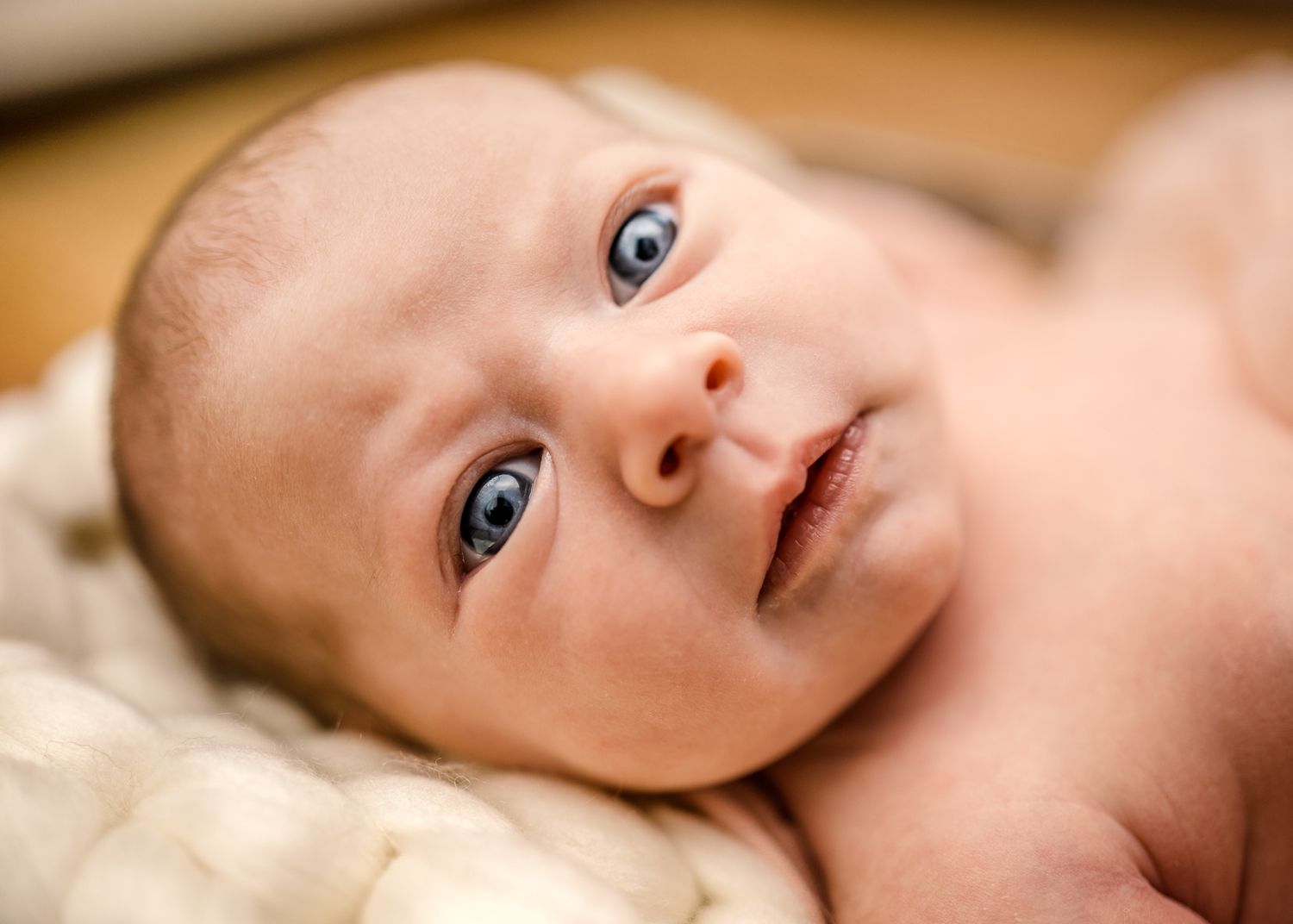 Close up of an infant lying on soft cream colored blanket.