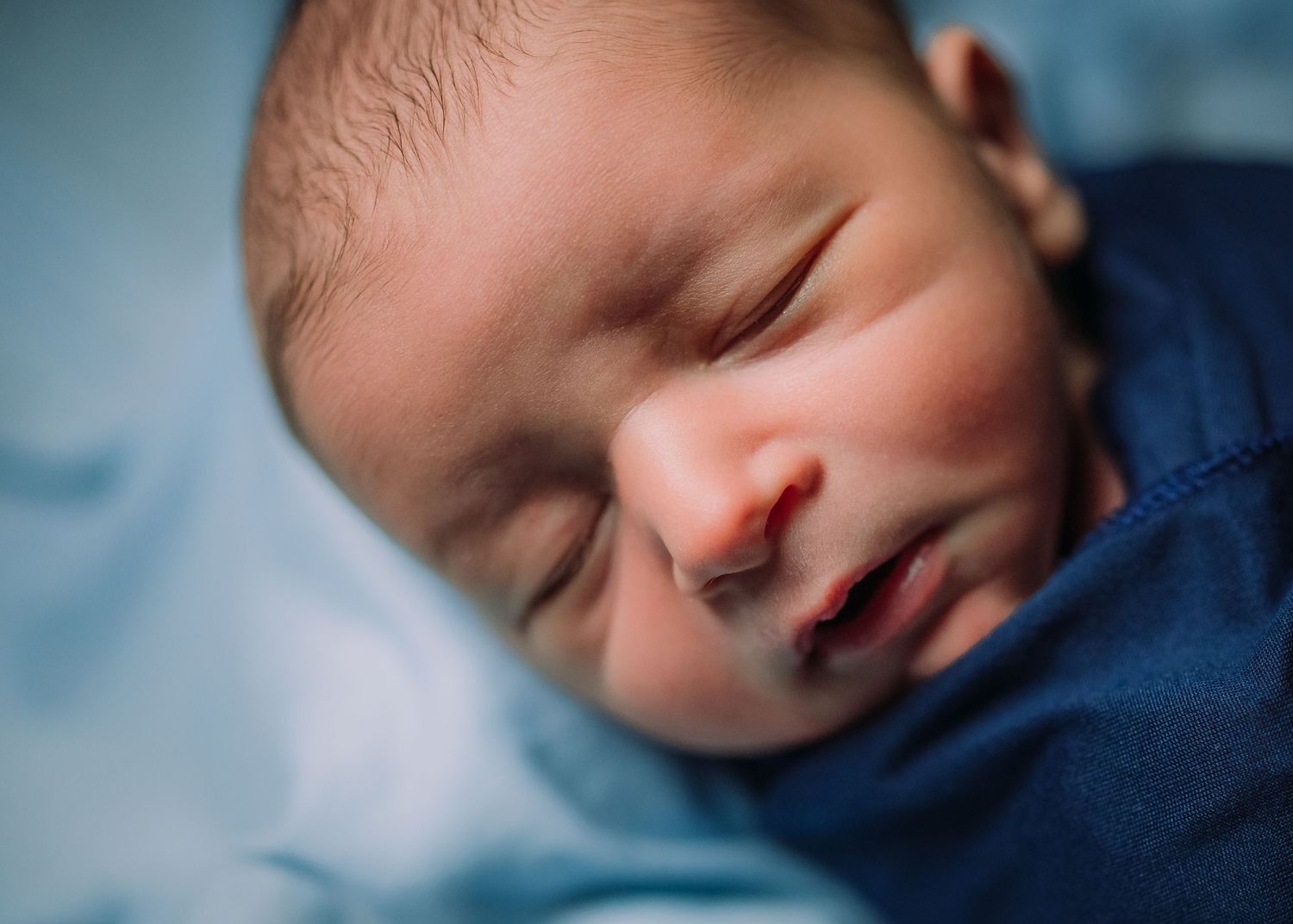Peaceful sleeping newborn baby in a navy blue outfit against soft blue background.
