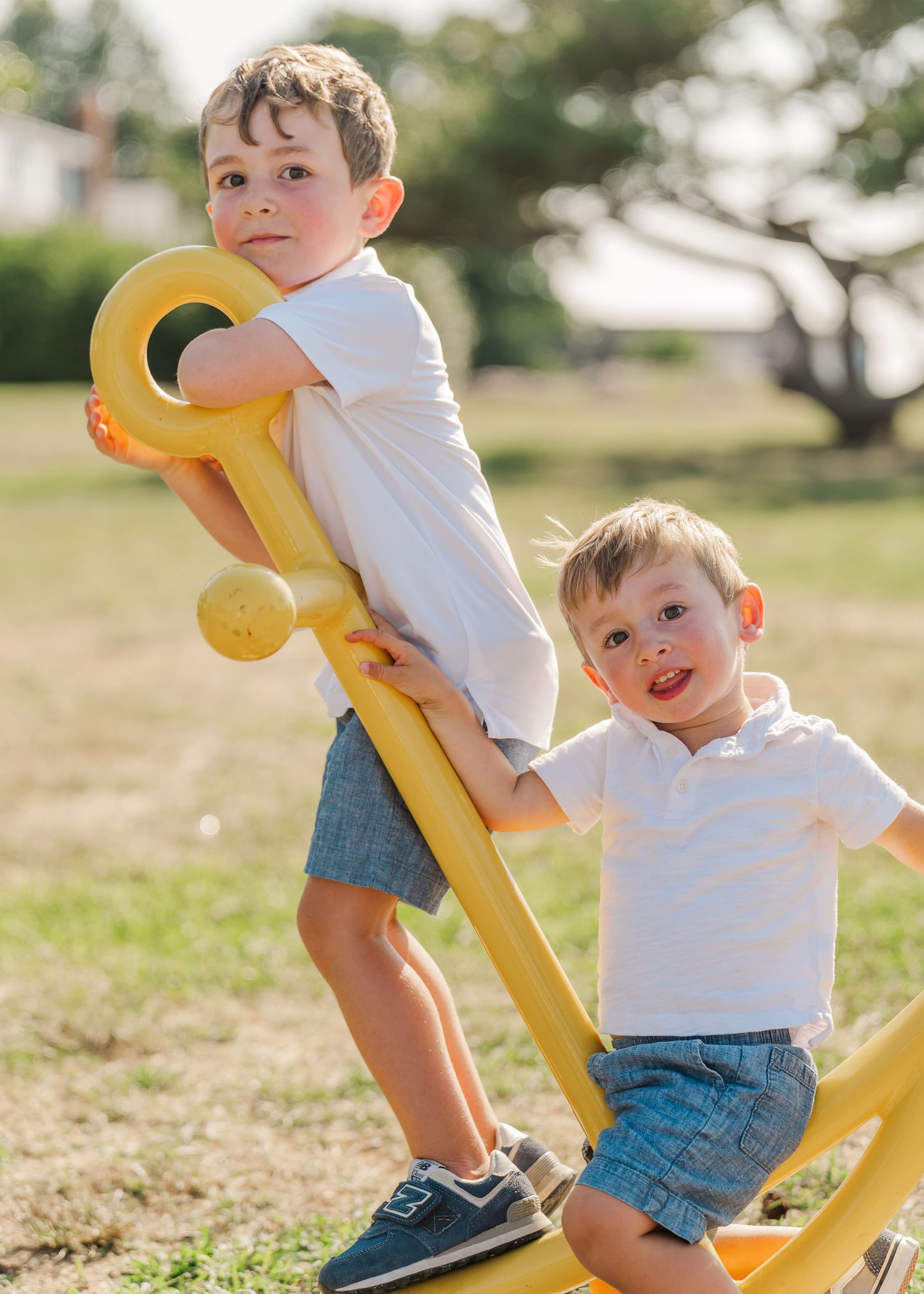 Two children playing together on a yellow outdoor seesaw in a sunny park on a summer day.