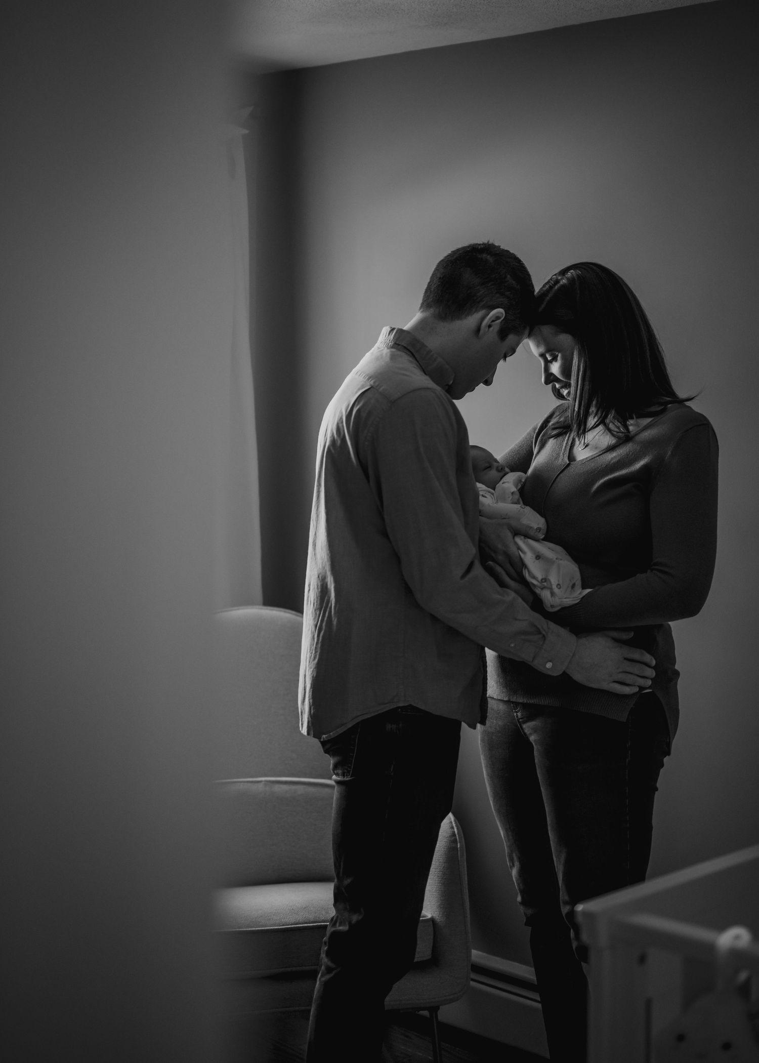 A black and white portrait of parents sharing an intimate moment with their newborn.