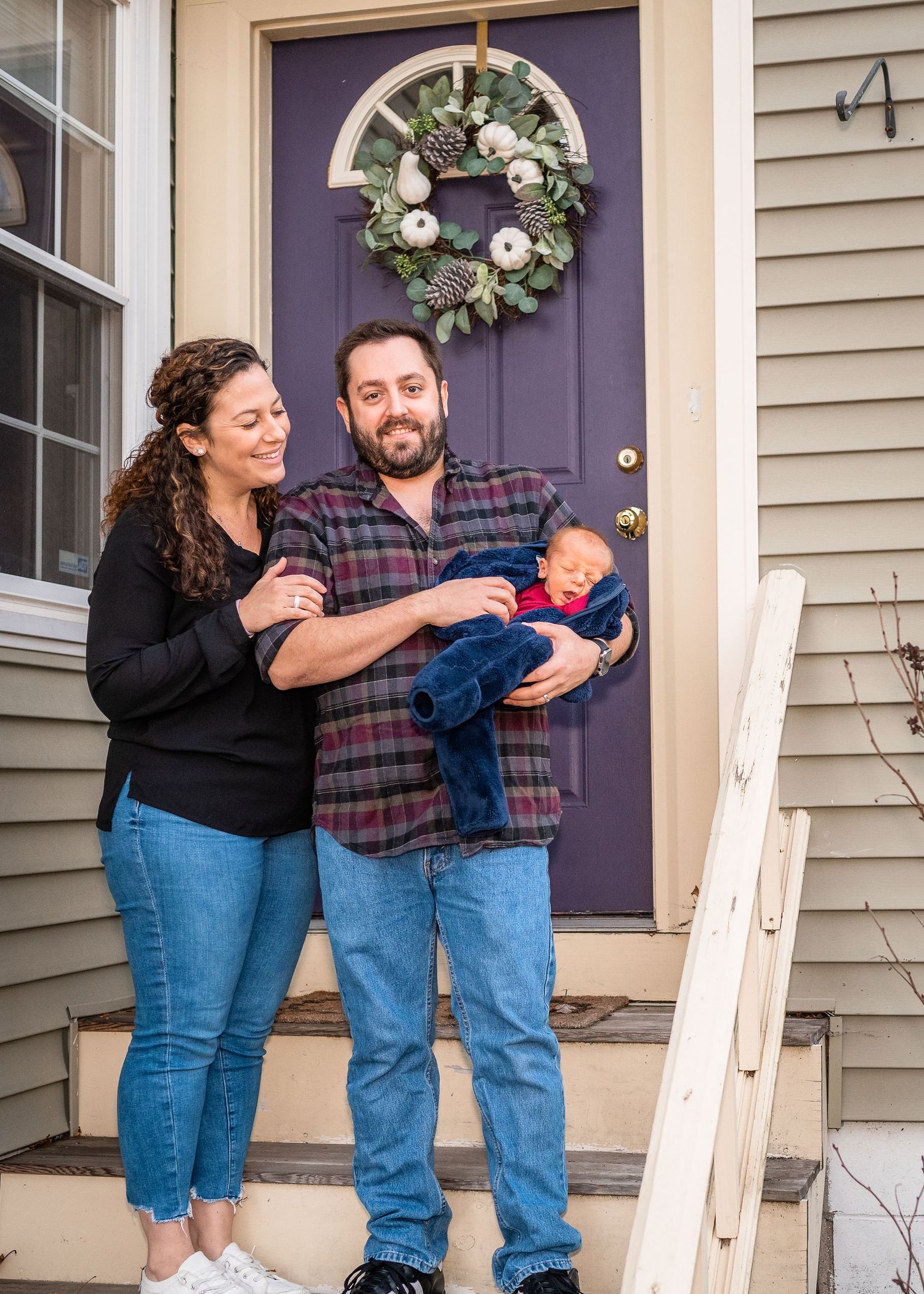 Family stands together on their front porch with a holiday wreath on purple door.