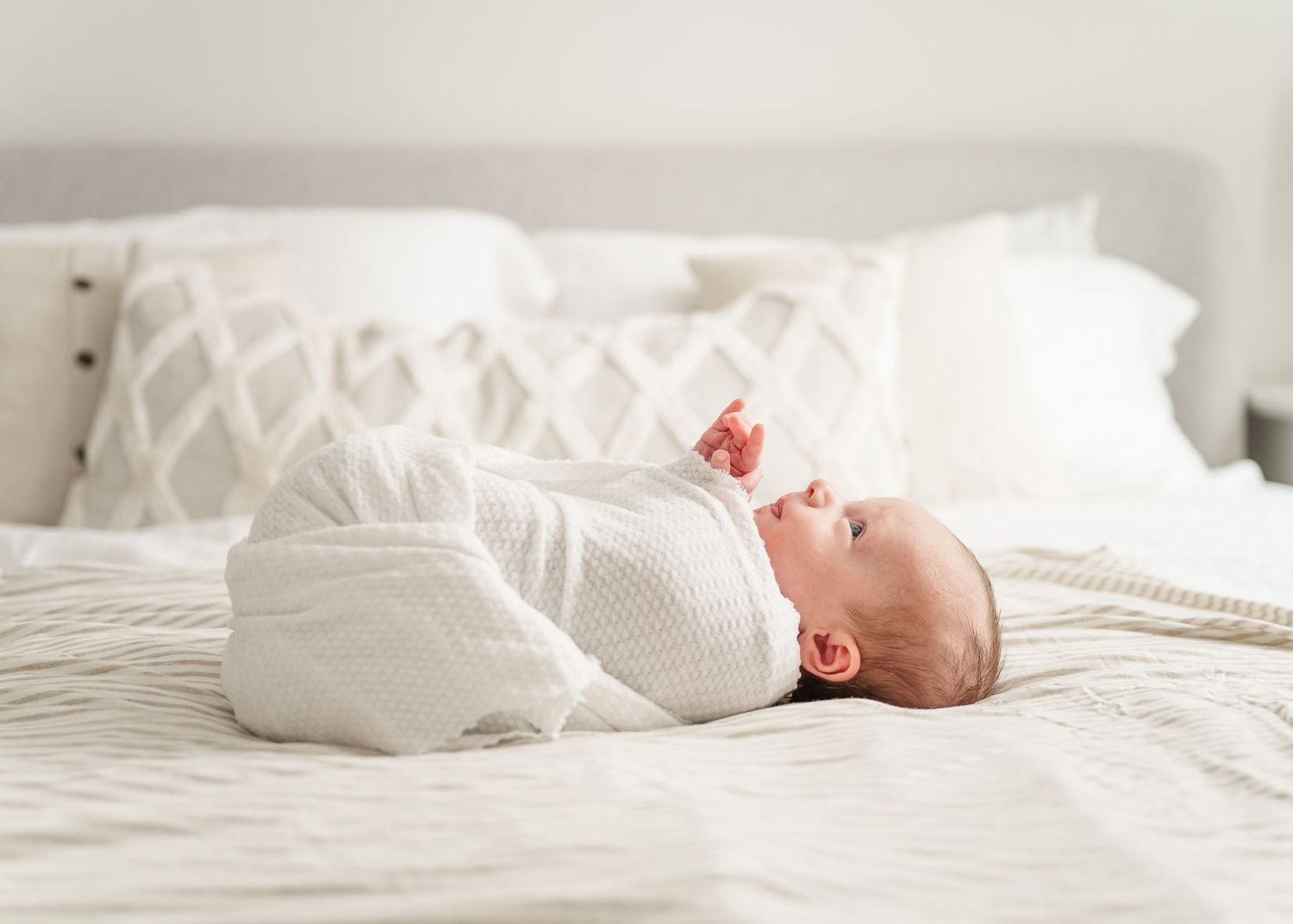 Infant lying peacefully on white bedding in a minimalist setting.