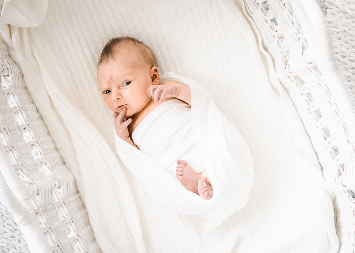 Baby wrapped in white blanket with feet visible against lace backdrop.