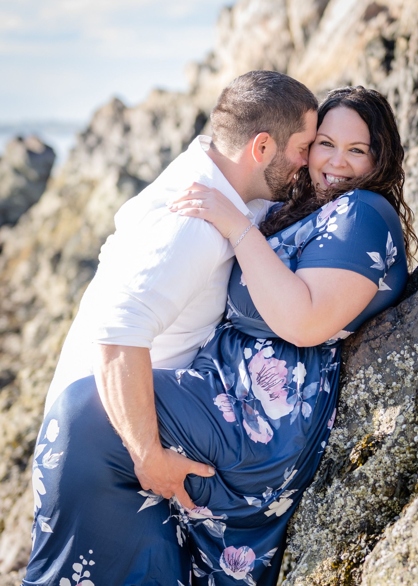 A tender moment captured between a couple against rocky coastal cliffs.