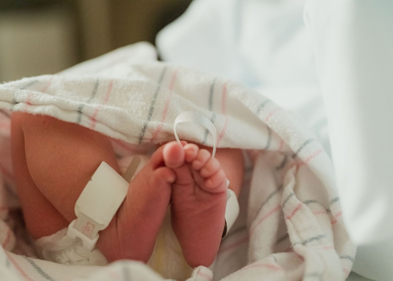 Tiny newborn baby feet wrapped in a white hospital blanket with a medical tag attached.