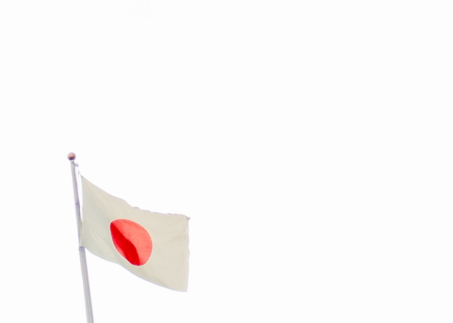 Japanese flag with red circle on white background flying against clear sky.