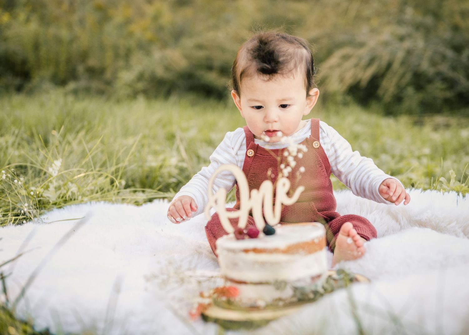 First birthday cake smash session outdoors with rustic decorations on white blanket.
