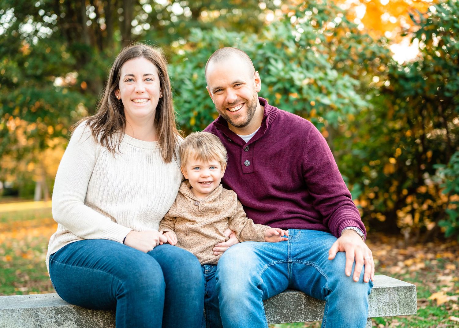 Family sitting together on stone wall during fall photo session with golden foliage.
