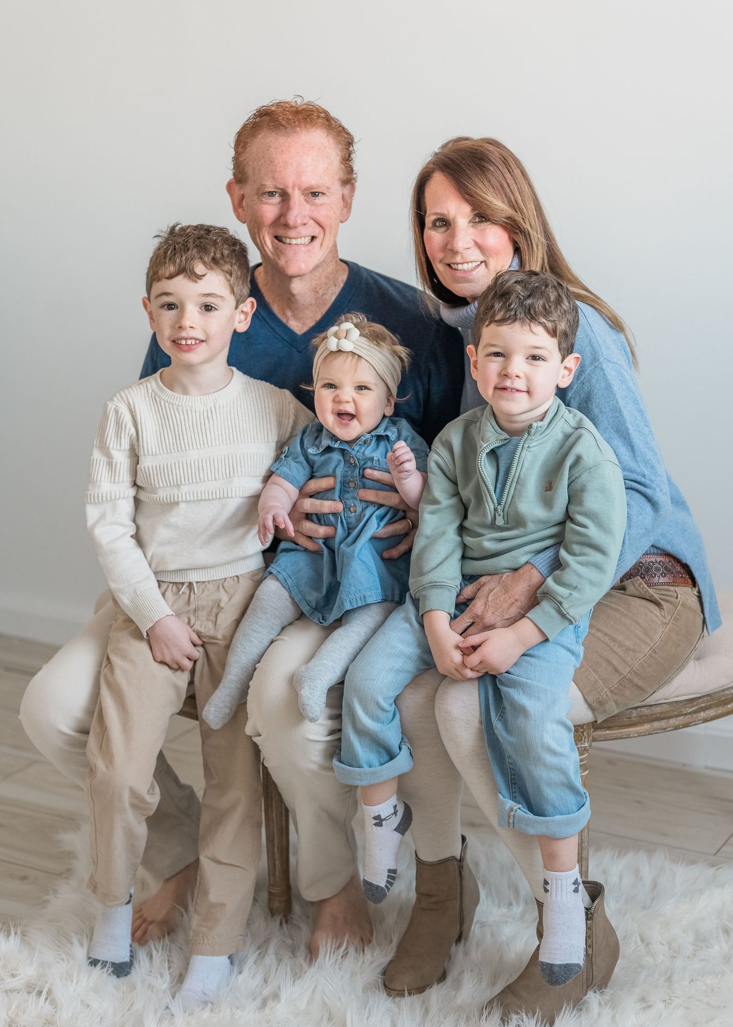 A family group poses on a white couch in matching casual outfits of blue and beige tones.
