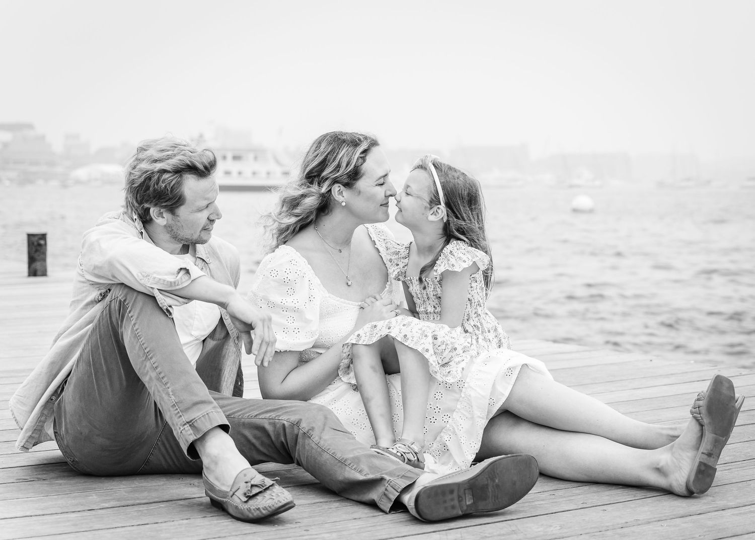 Black and white photo of a family sharing a tender moment while sitting on a dock.