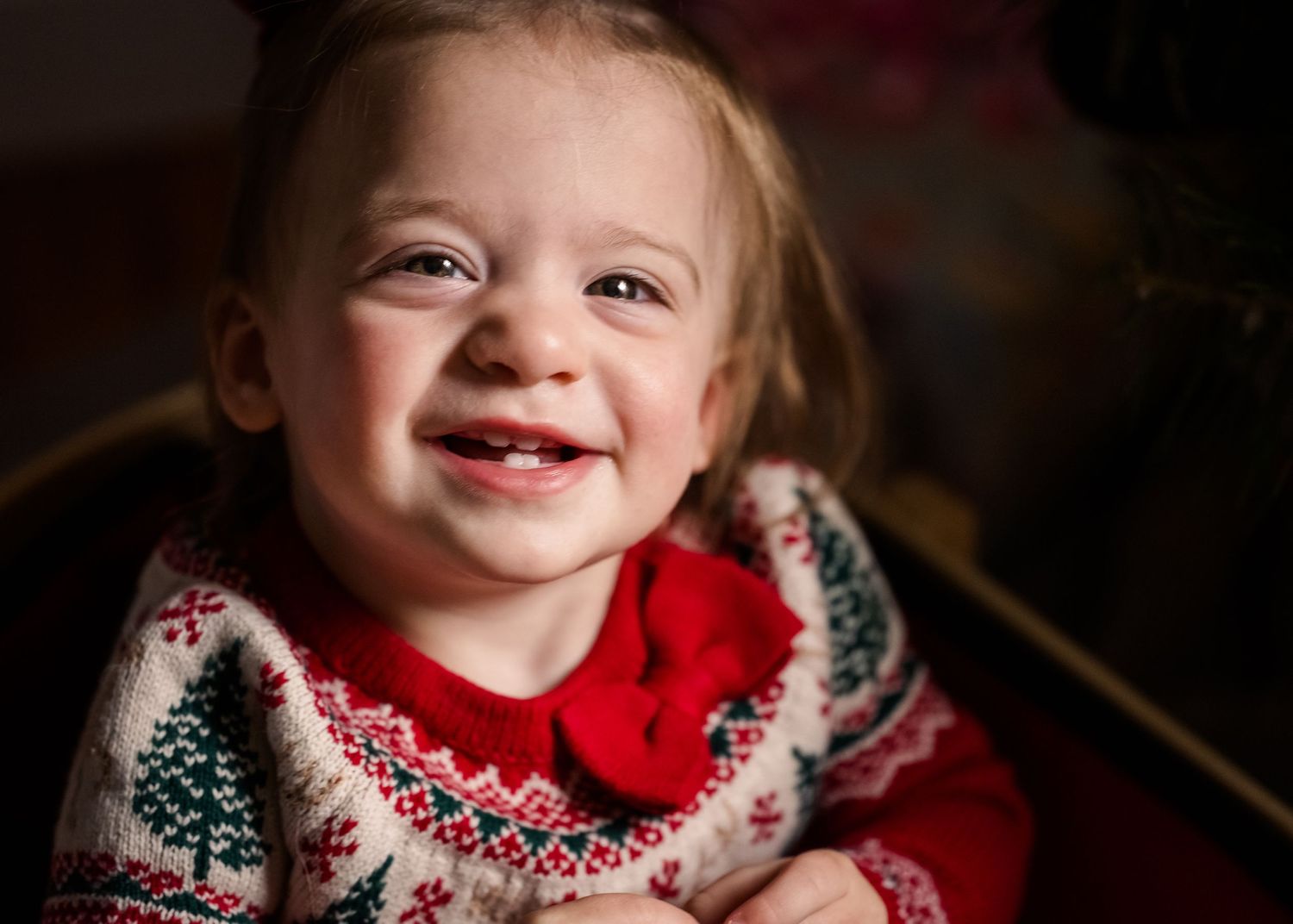 Holiday portrait featuring festive sweater and joyful expression by Christmas tree.