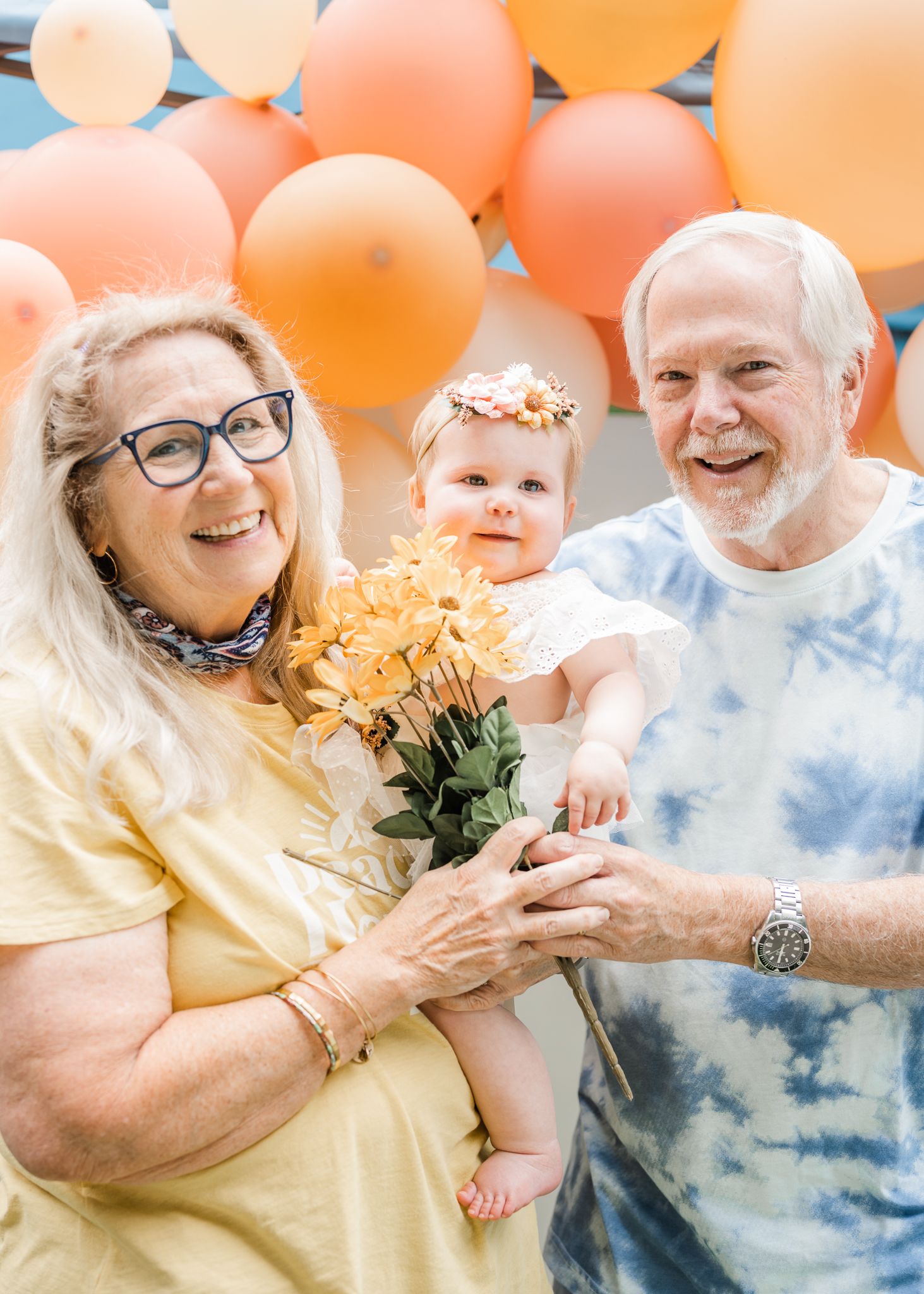 Family portrait with peach balloons and yellow flowers creating cheerful backdrop.