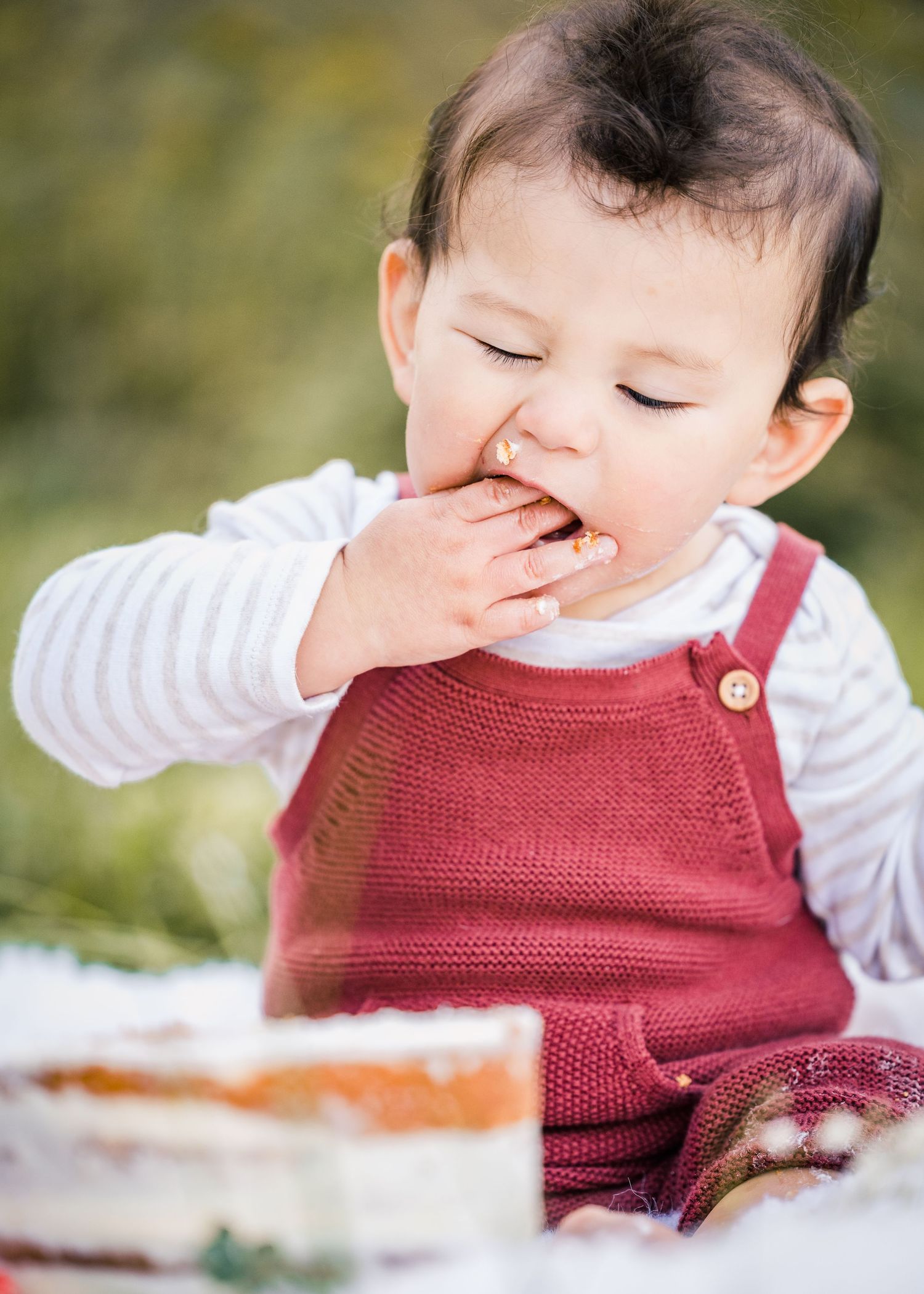 Close up portrait of baby enjoying cake during outdoor first birthday session.