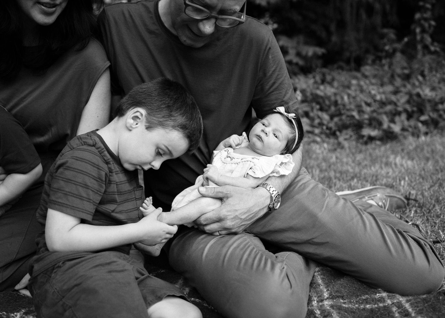Black and white photo of family bonding moment on blanket outdoors.