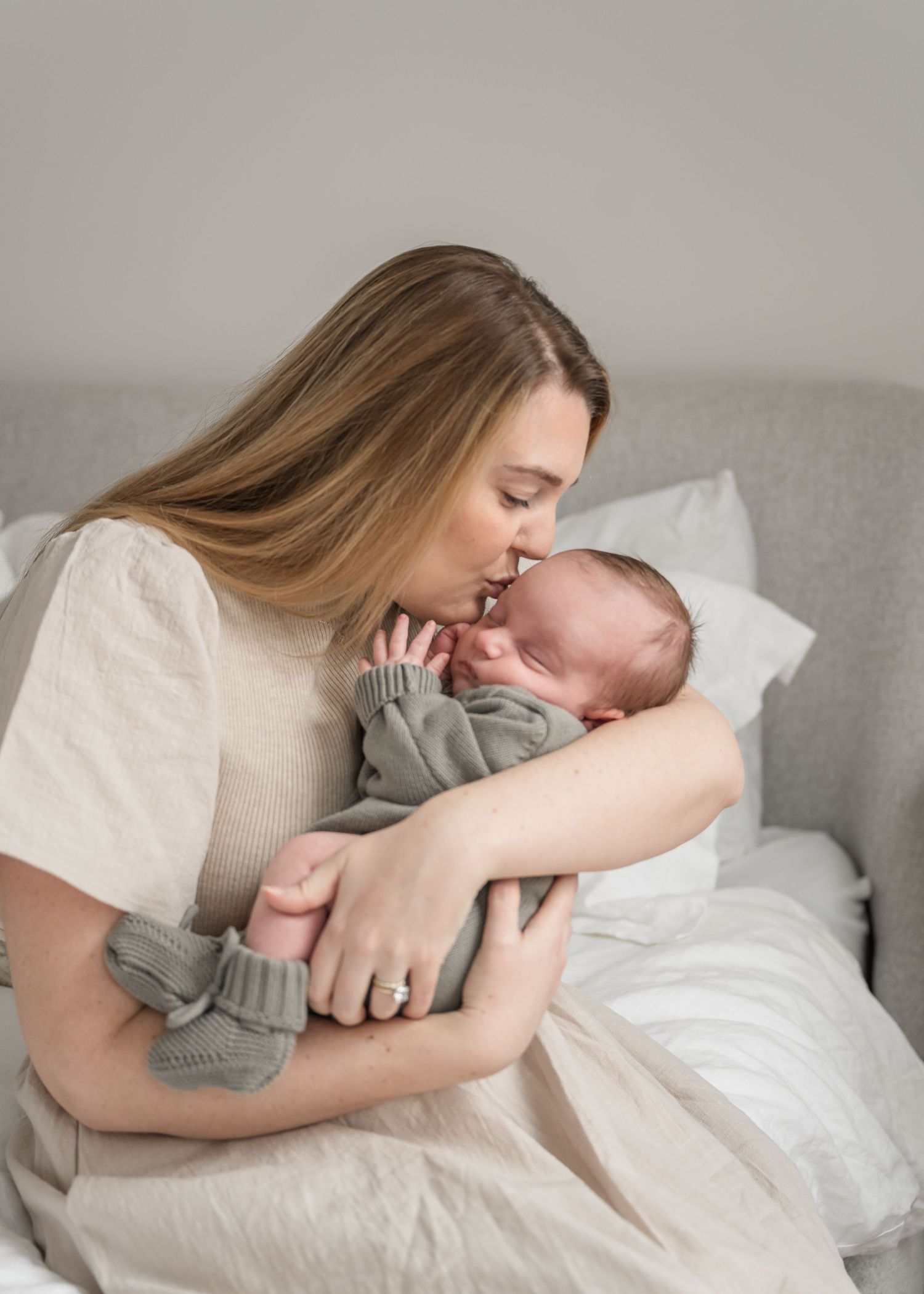 Intimate moment between parent and newborn baby on a light gray couch with white pillows.
