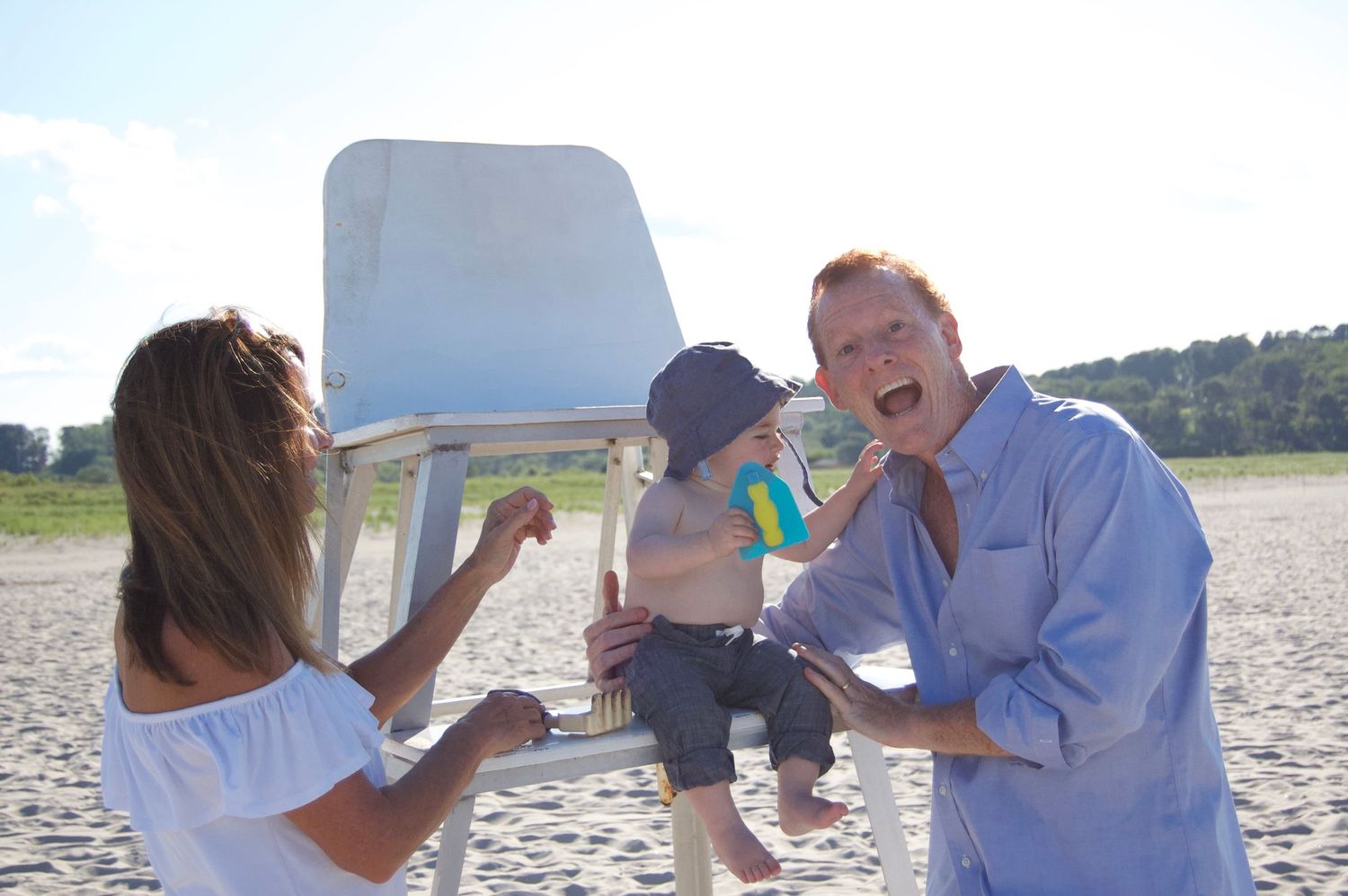 Family playing together and laughing on a sandy beach.