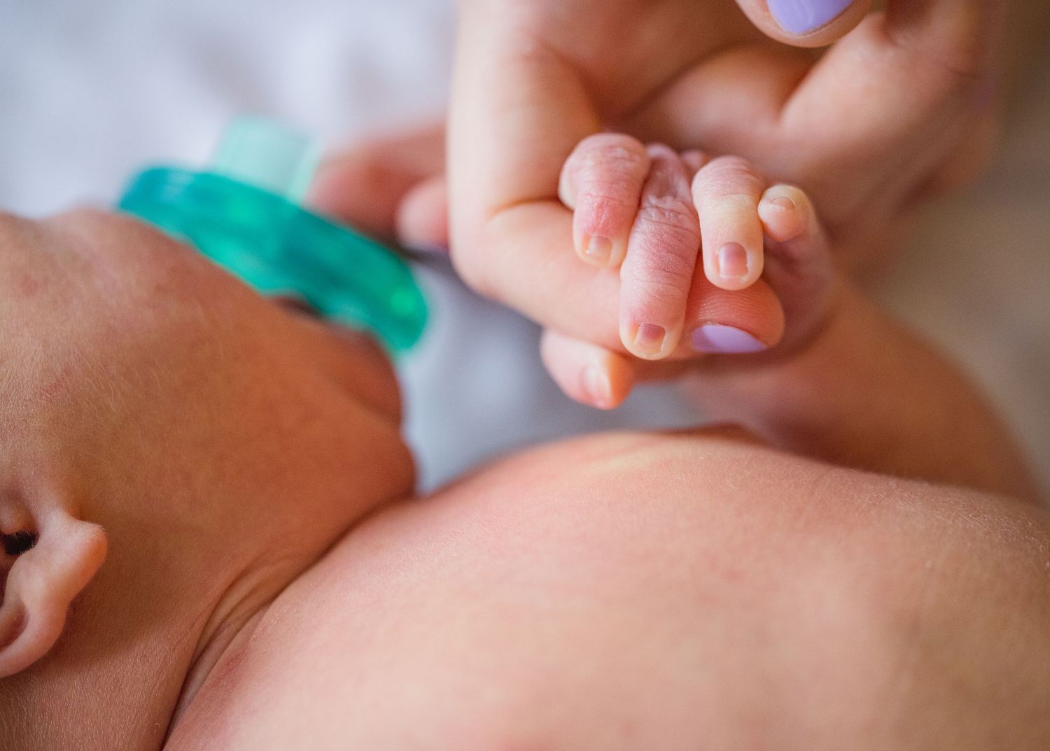 Gentle touch of tiny newborn fingers with pacifier visible.