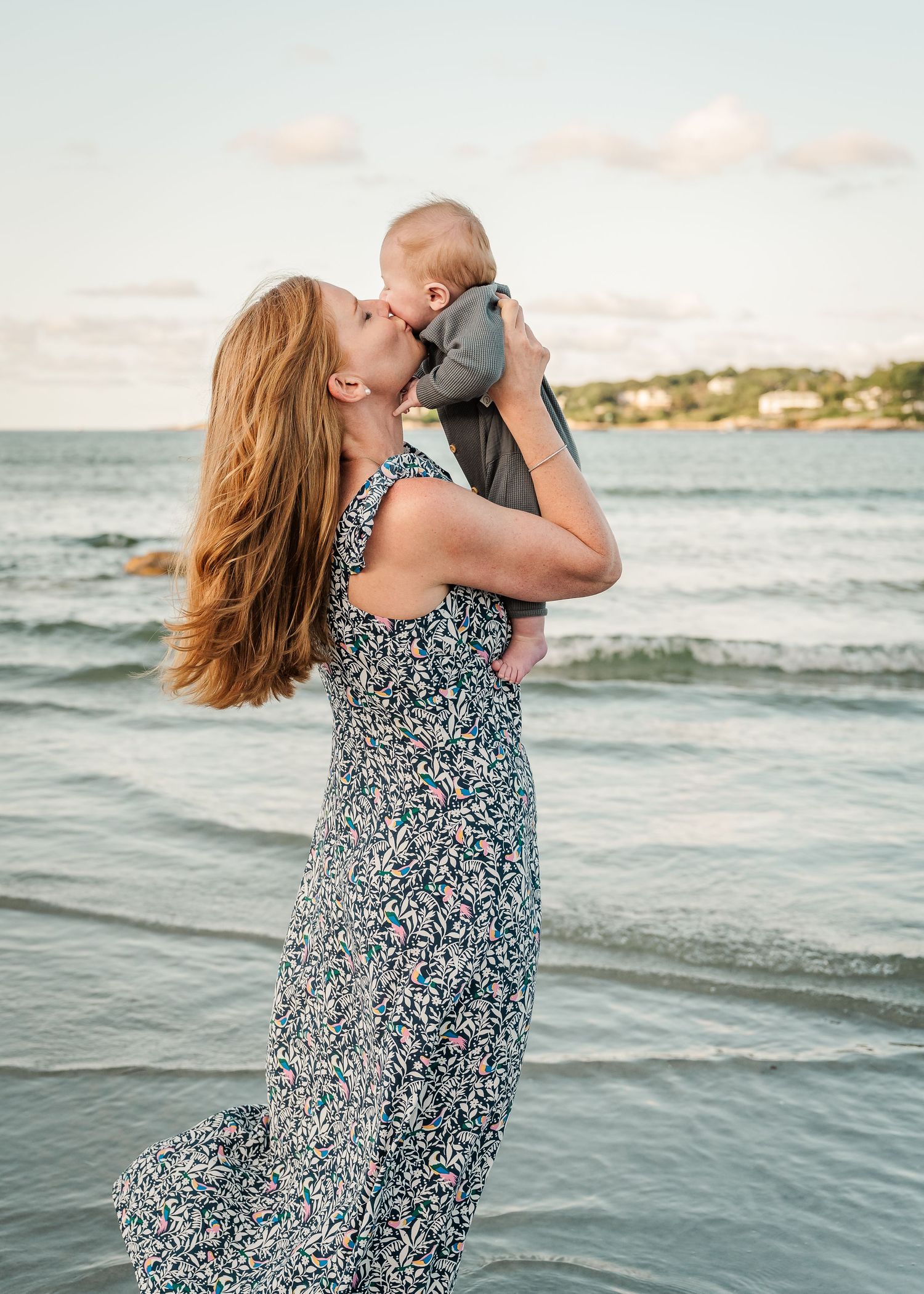 A tender moment shared between parent and baby at sunset on a beach with gentle waves rolling in the background.