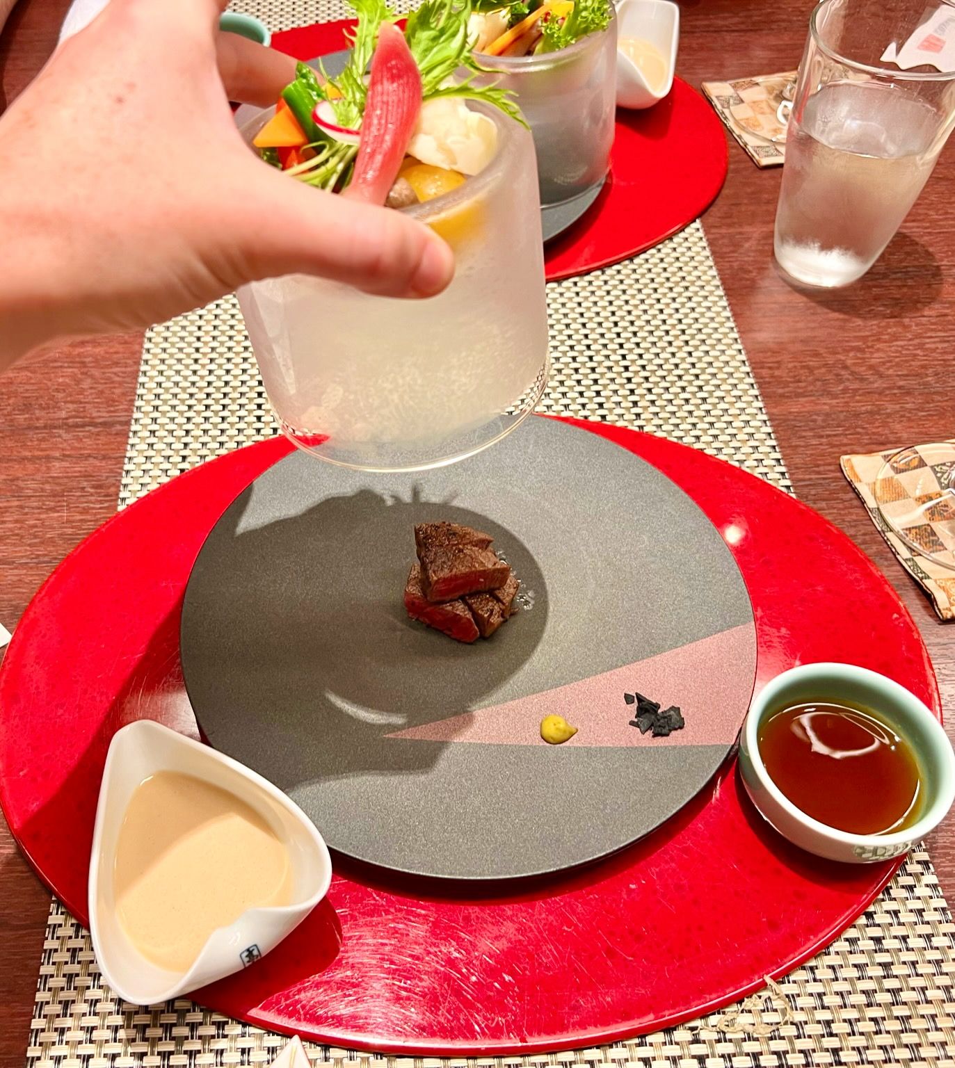 An artistic Japanese bento box arrangement featuring nine compartments of colorful dishes and soups.
