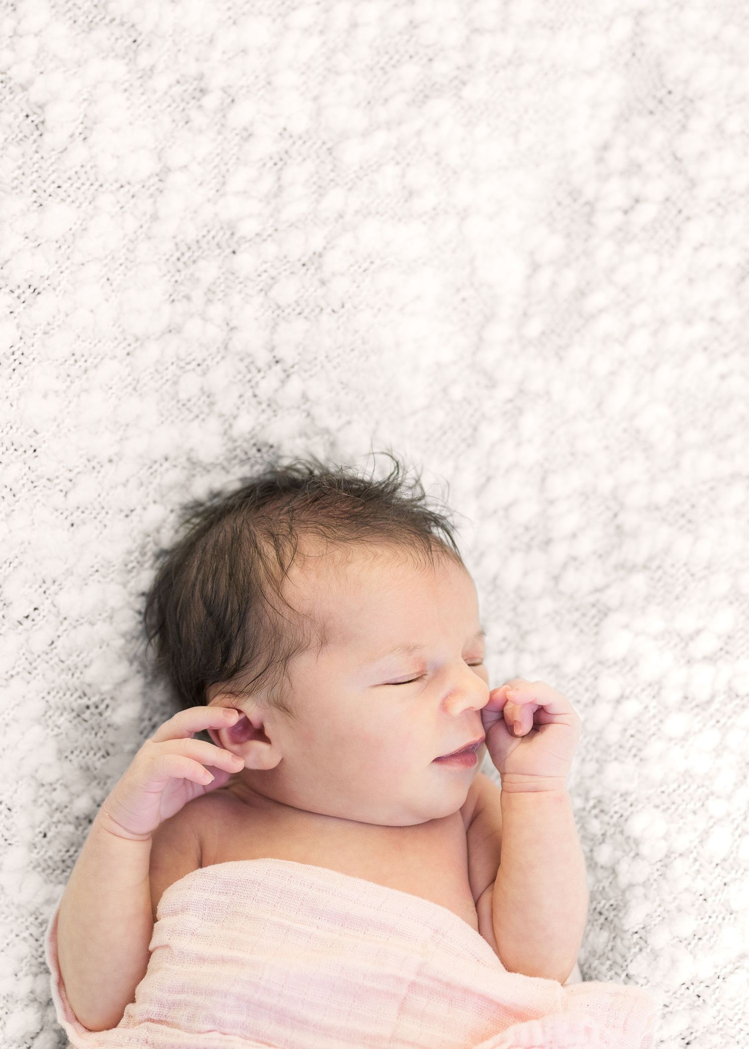 Sleeping newborn wrapped in pink swaddle on textured white background.