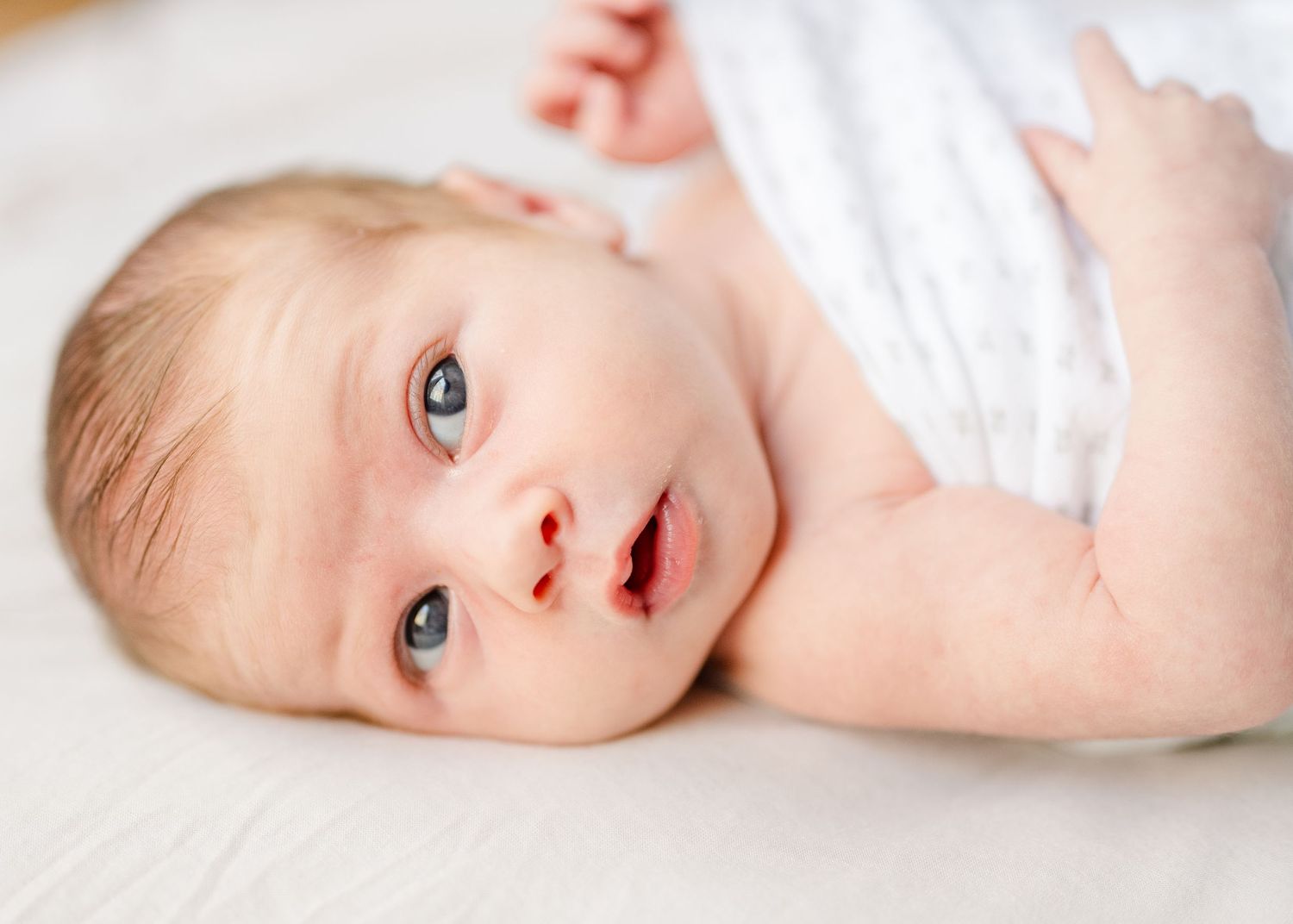 Sweet baby in white blanket with bright blue eyes looking directly at camera.