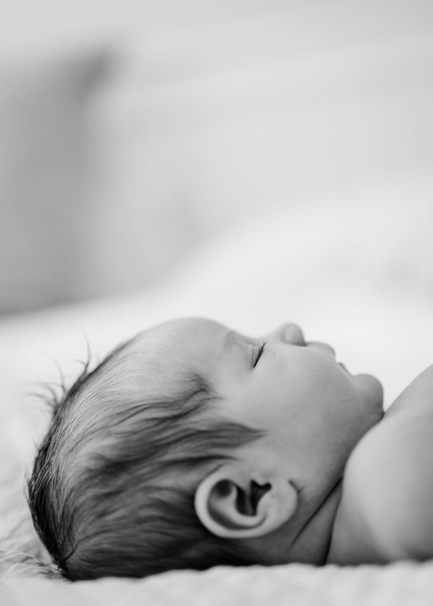 Black and white close-up shot of a sleeping baby lying down with visible ear and dark hair in peaceful repose.