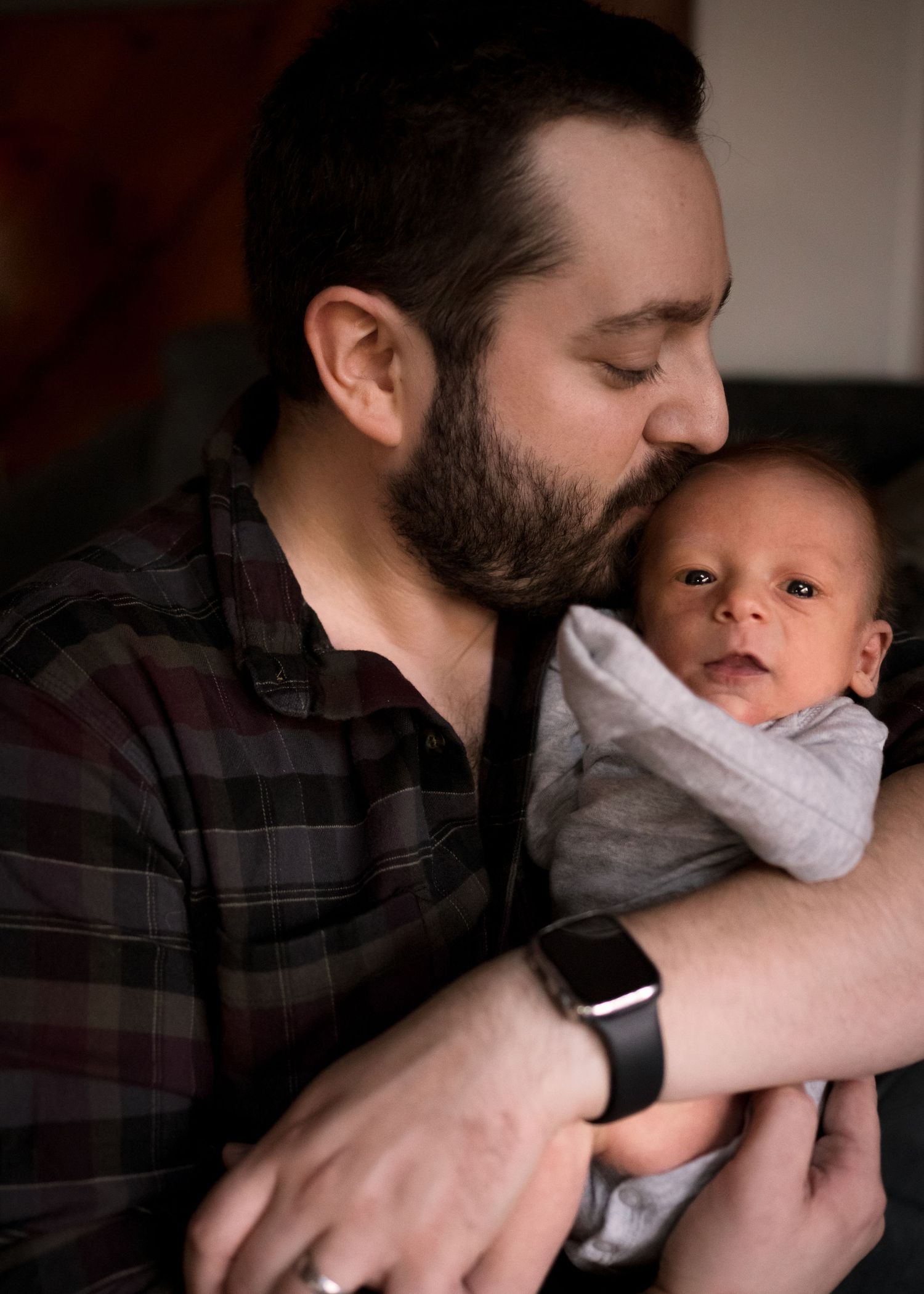 Tender moment between father in plaid shirt and newborn baby.