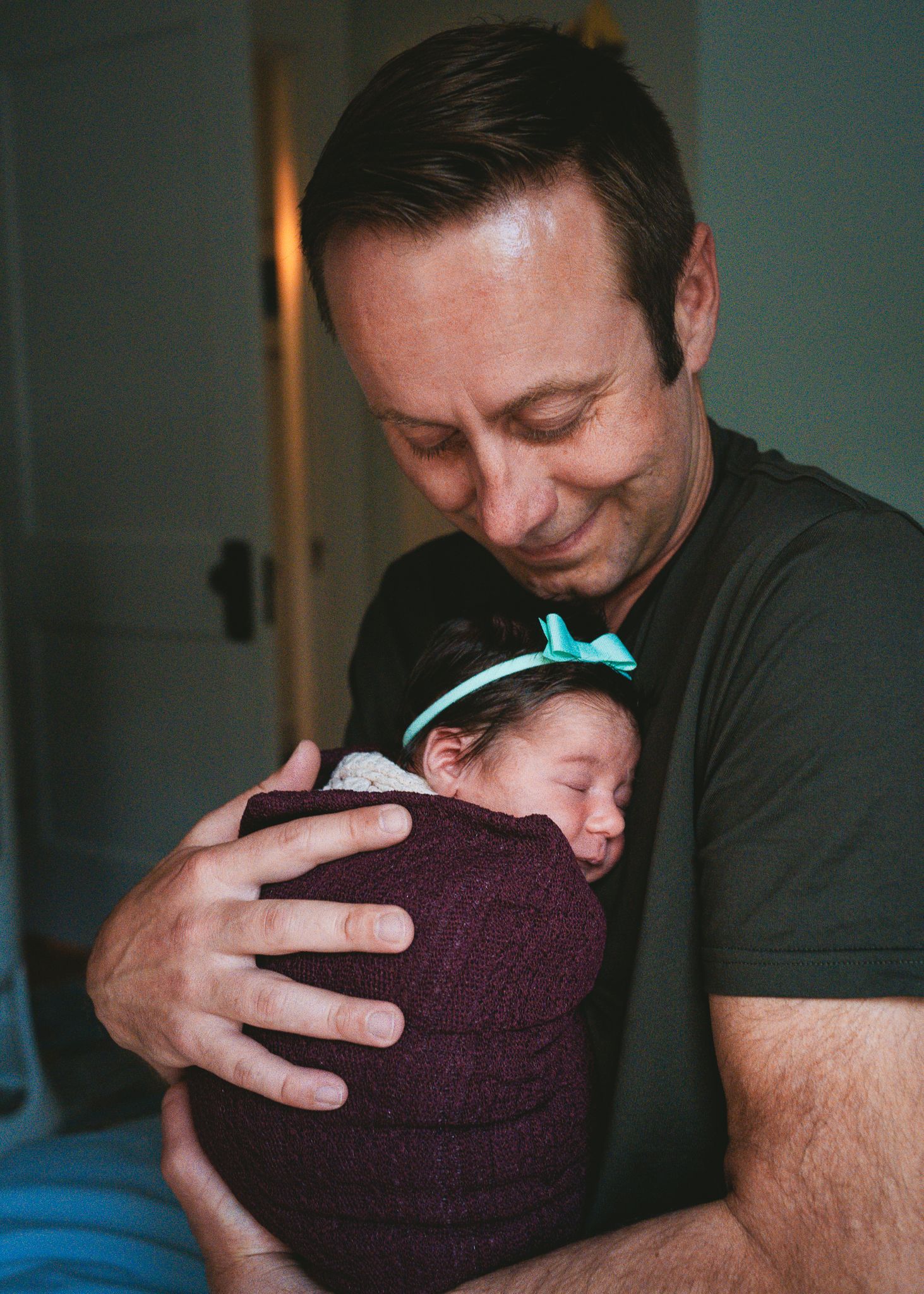 Person holding sleeping newborn wrapped in burgundy swaddle with mint bow.