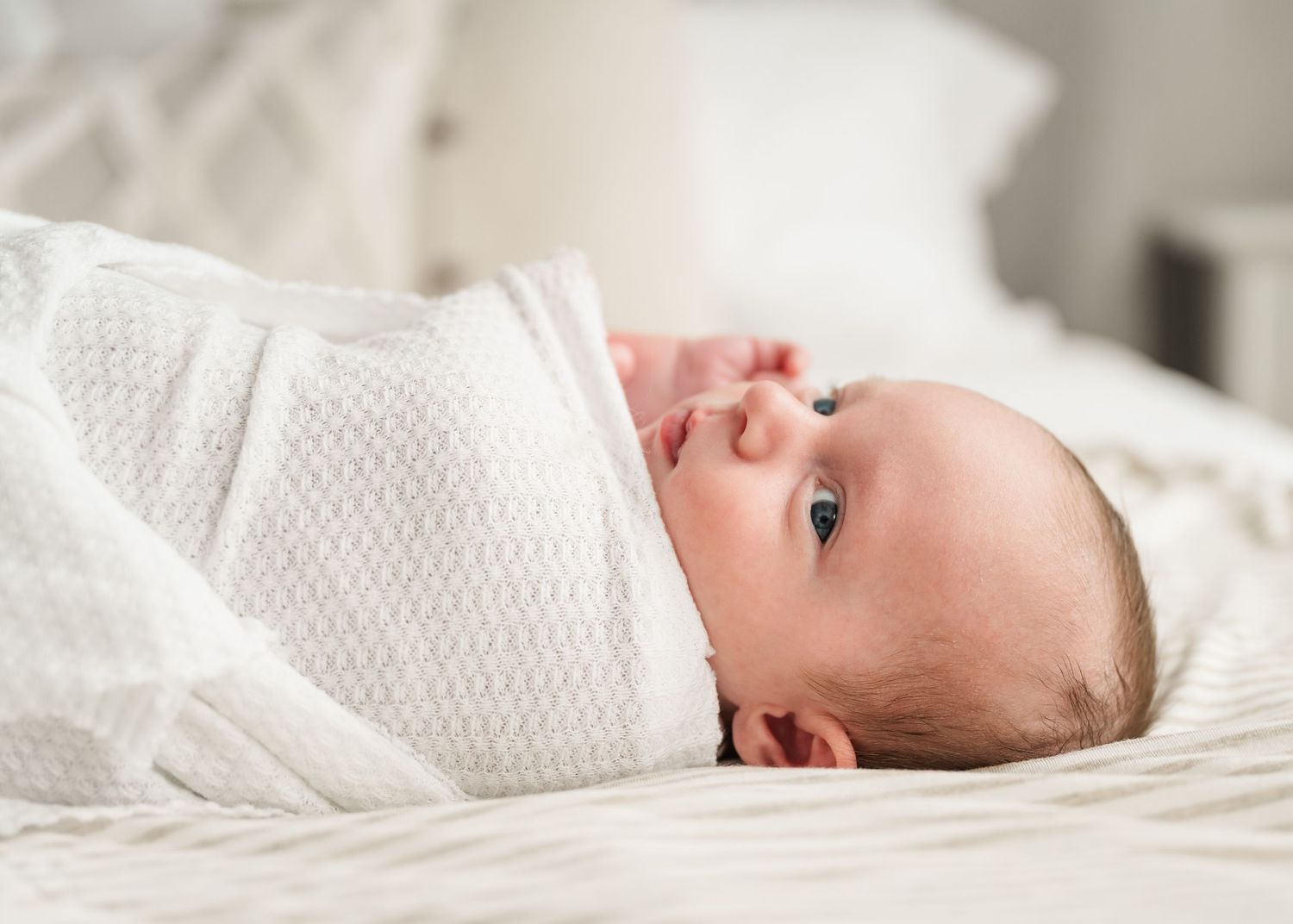 Minimalist photos of newborn baby resting on textured white bedding.