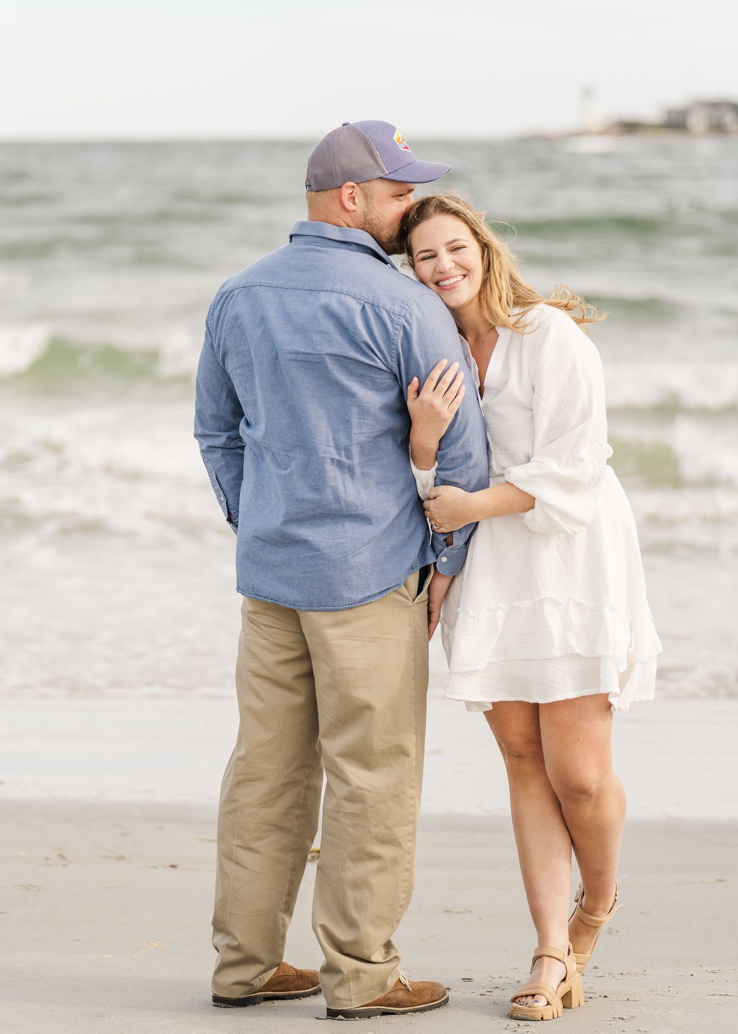 A tender moment between a couple standing on the beach with waves in the background.