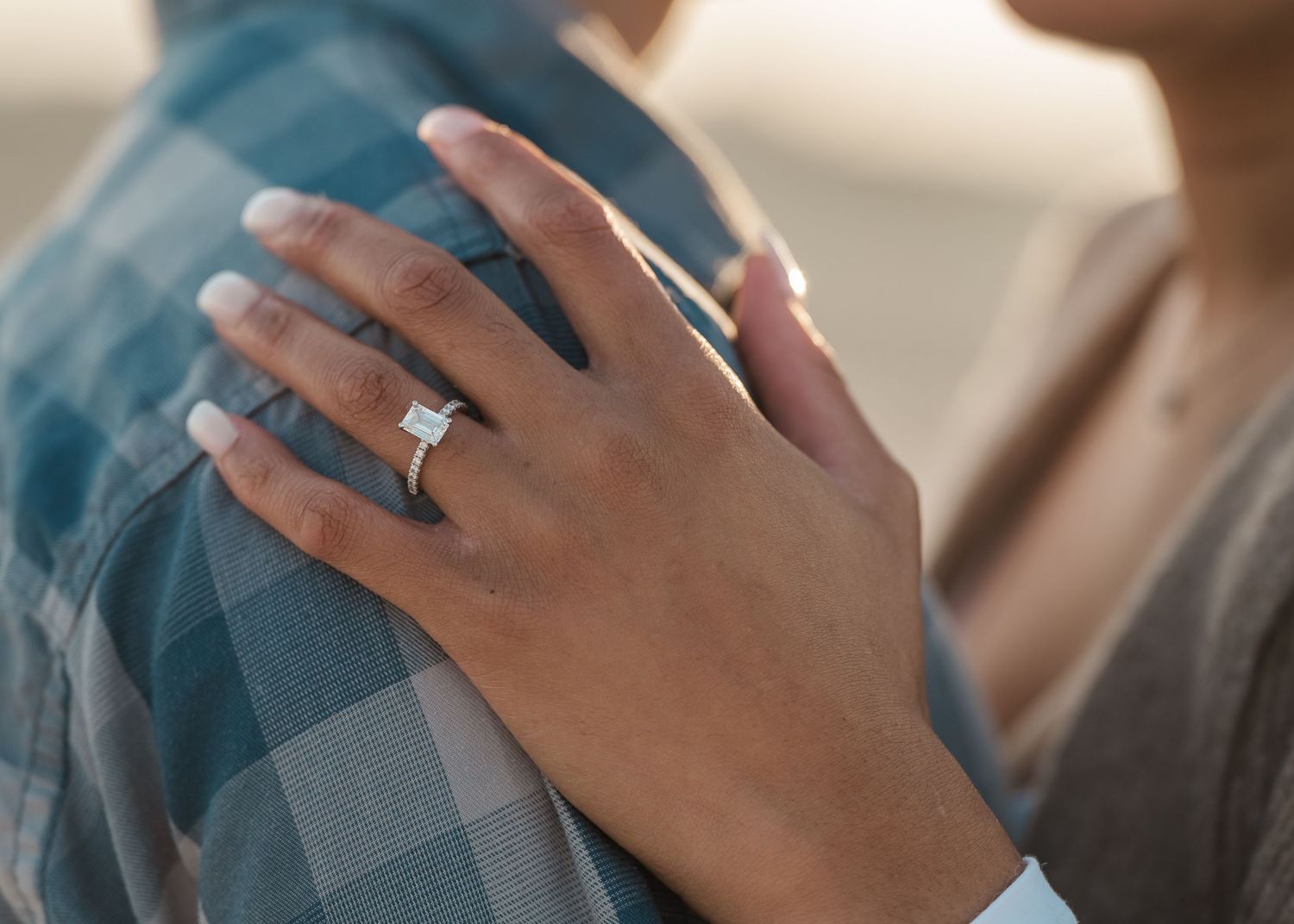 Close-up shot of hands showing off a new engagement ring against a plaid shirt.