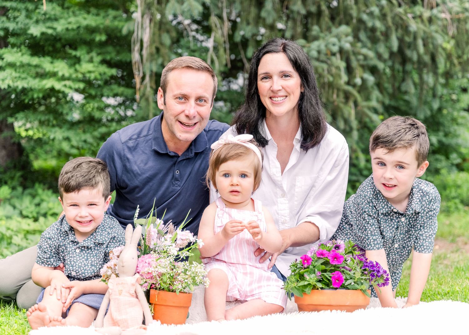 Outdoor family photo session with potted flowers and greenery in the background.