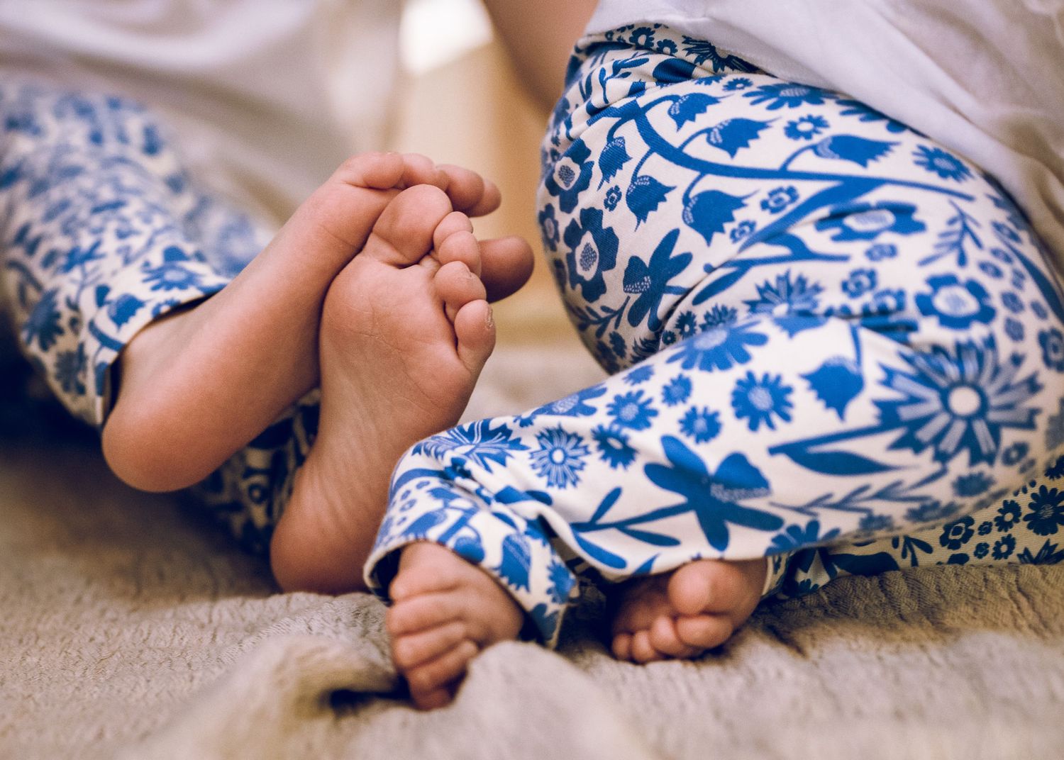 Close-up of tiny feet wearing blue and white patterned leggings on a soft gray surface.