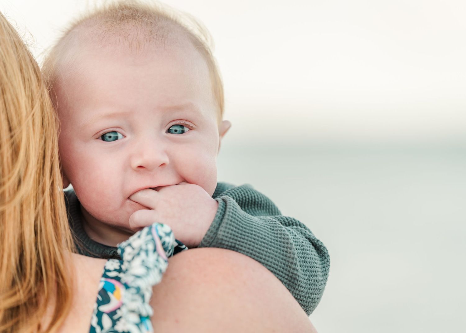 A baby in a green sweater rests against someone wearing white and blue on a light background.