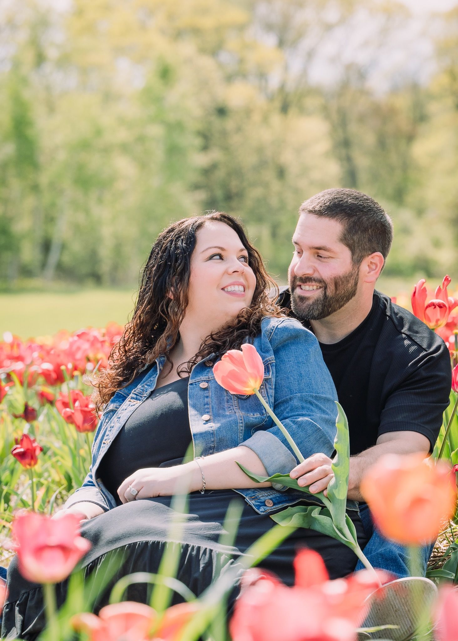 Romantic couple sitting among blooming tulips during spring photo session.