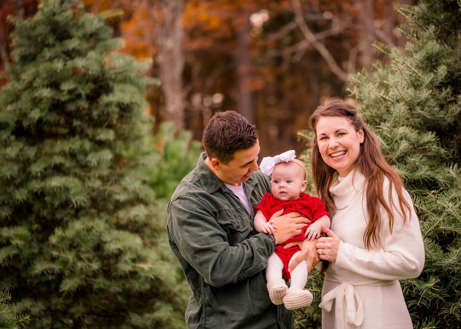 Family poses together among evergreen trees during fall season.