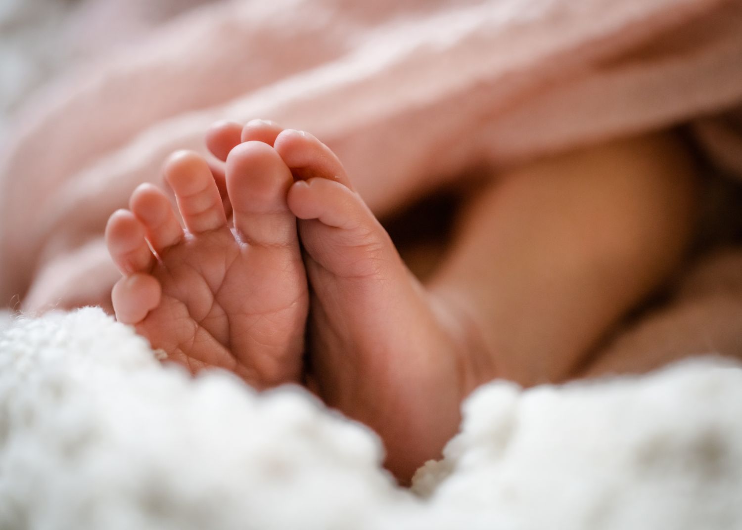 Tiny newborn baby feet resting on soft white blankets in gentle natural lighting.
