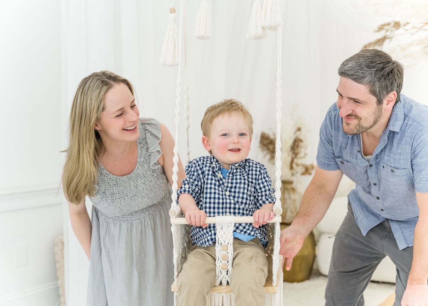 A family enjoys playing together on an indoor swing in a bright white room during a lifestyle photo session.
