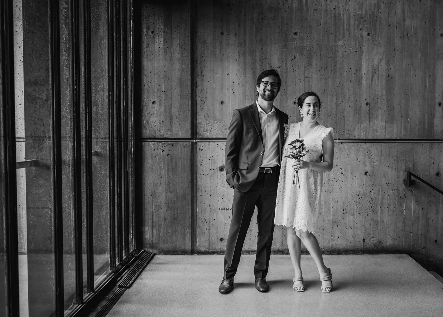 A black and white portrait of a couple standing in an industrial modern building interior.